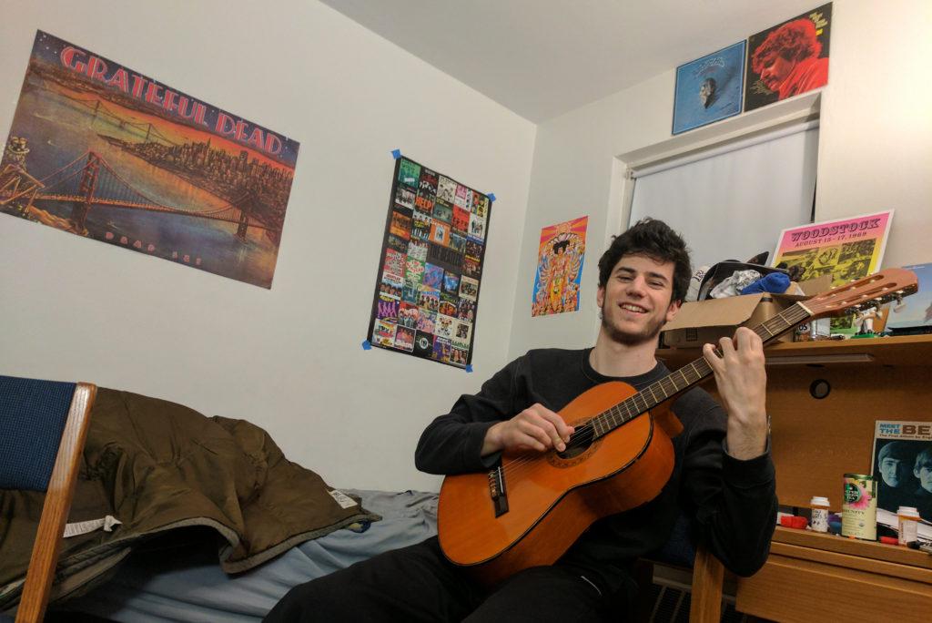 Jacob Hill ’19 of “Vinyl Fridays” demonstrates his guitar skills in front of his classic rock posters. Photo by Nieberg ’19.
