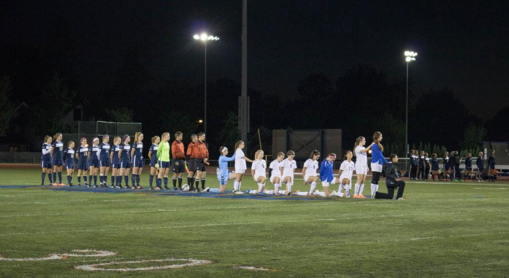 Members of the Macalester Women’s Soccer team kneel in protest during the playing of the national anthem before their game 
against Carleton College on Wednesday, Oct. 4. The Scots and Knights tied 1-1. Photo by Josh Koh ’18. 